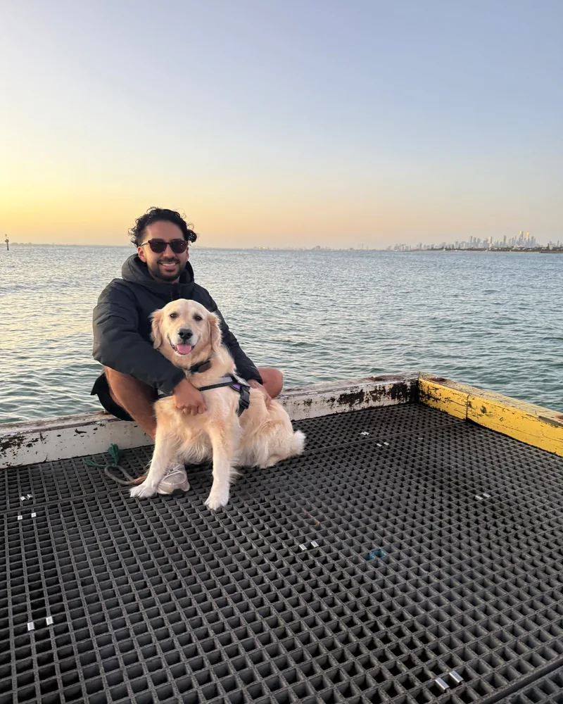 Nico sitting on a pier at sunset with a golden retriever, the city skyline across the water
