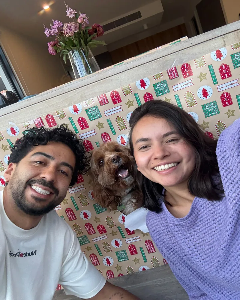 Yen and Nico with a red cavoodle in front of Christmas wrapping paper