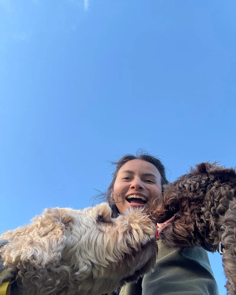 Yen laughing between two curly dogs against a clear blue sky